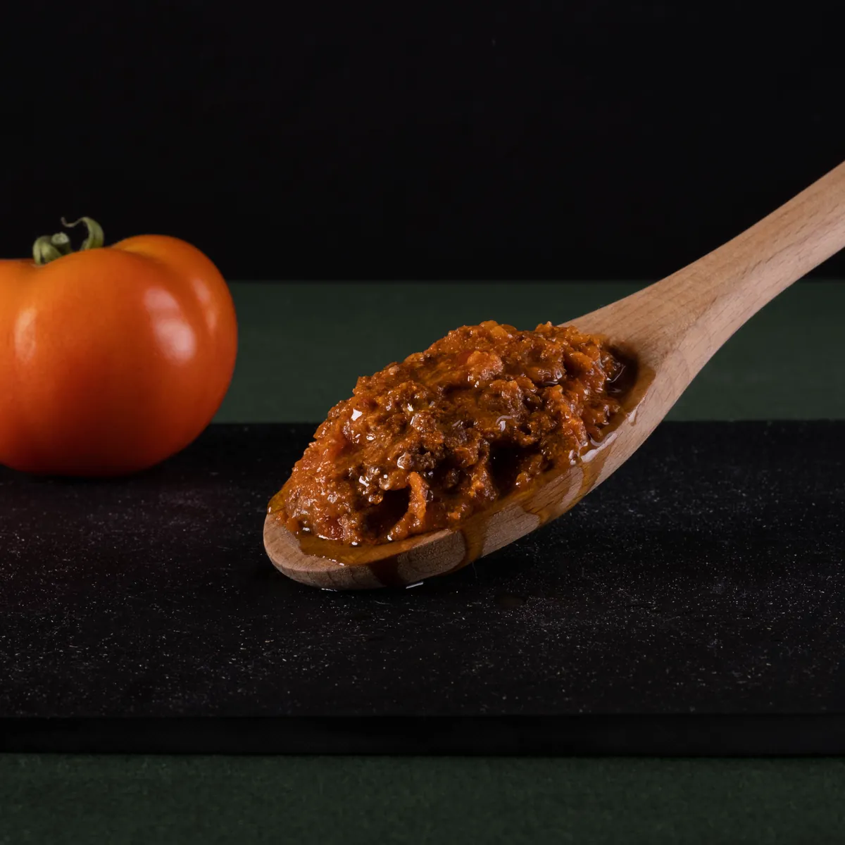 Cucchiaio di legno con sugo accanto a un pomodoro