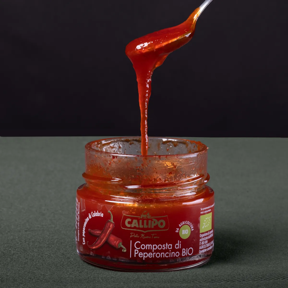 Cucchiaio che cola composta di peperoncino in un vasetto Callipo