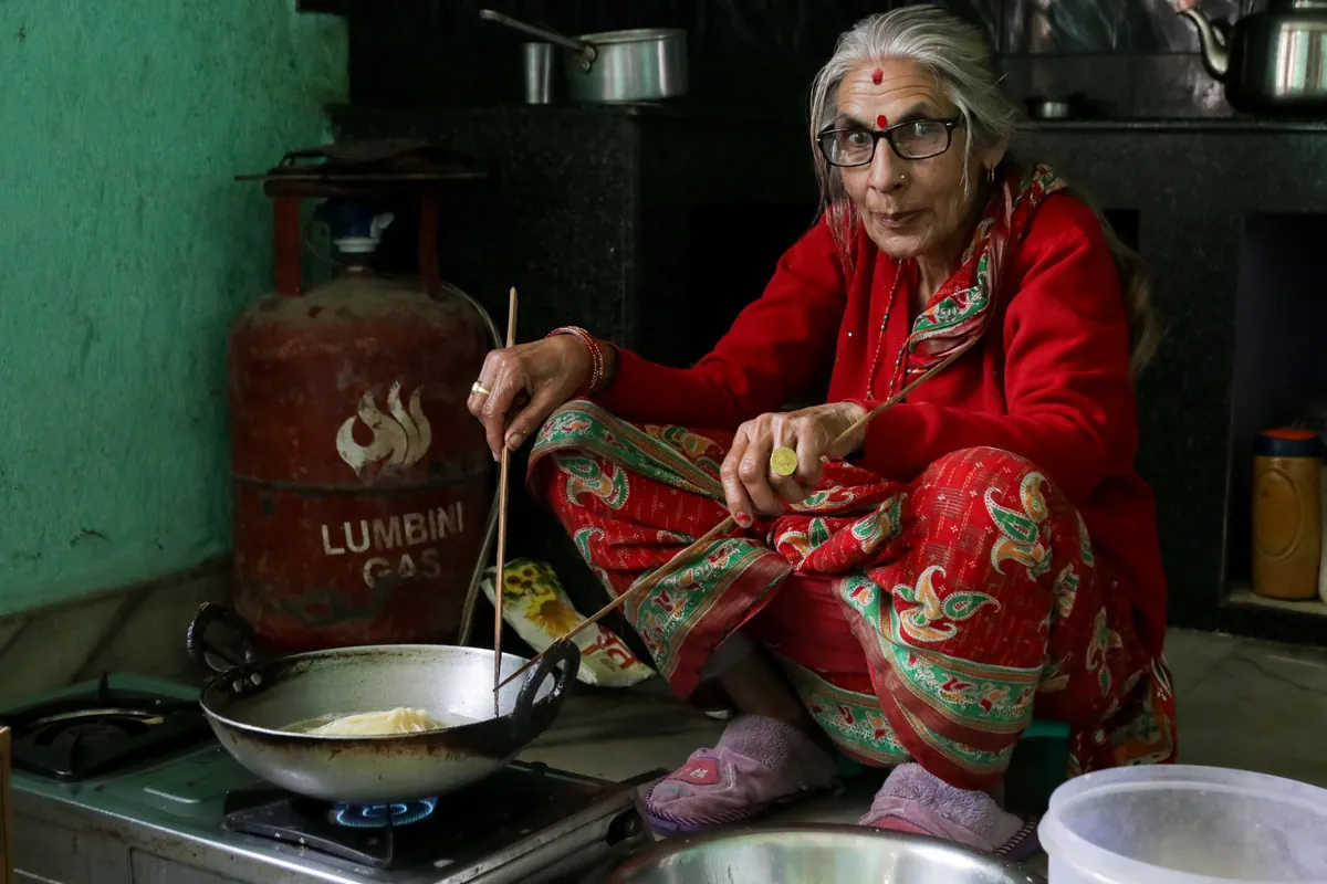 Anziana in abito rosso che cucina su un fornello a gas