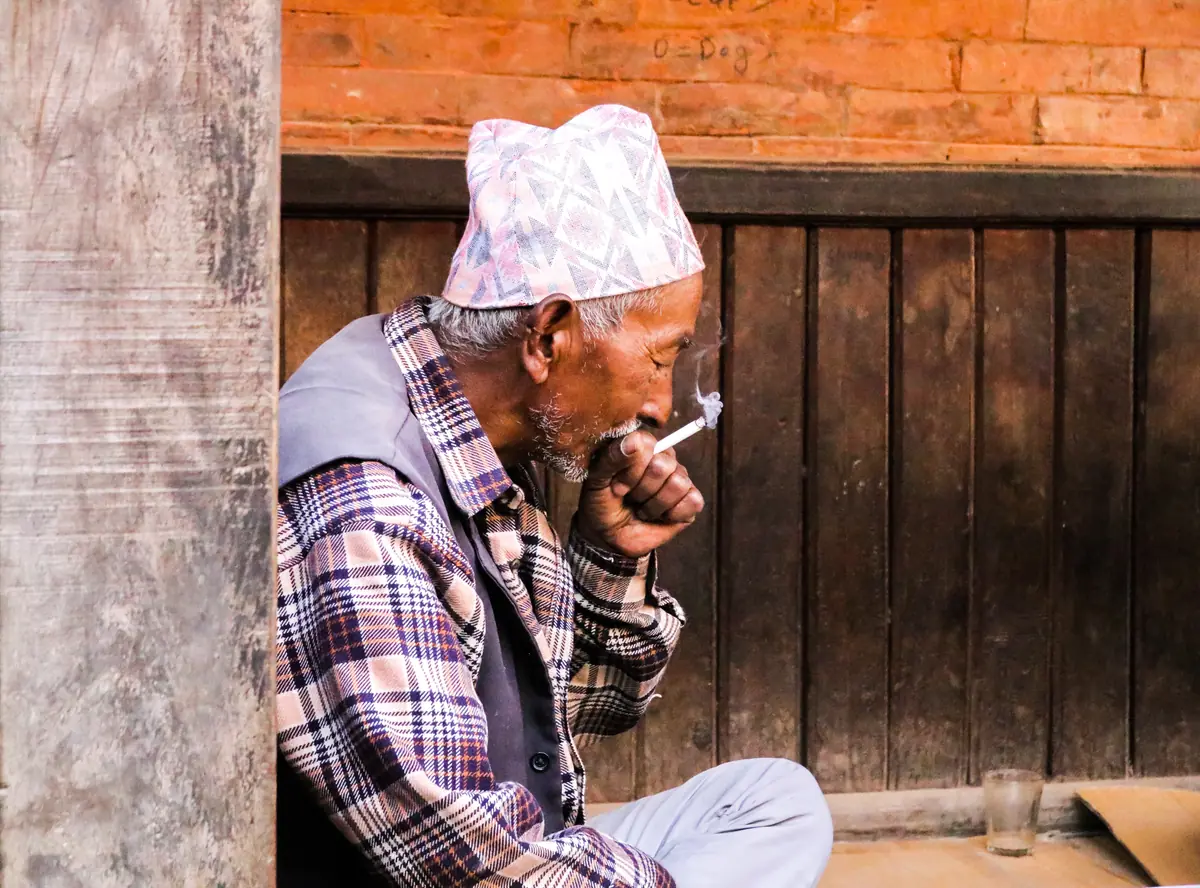 Anziano con il cappello tradizionale che fuma seduto davanti a una porta