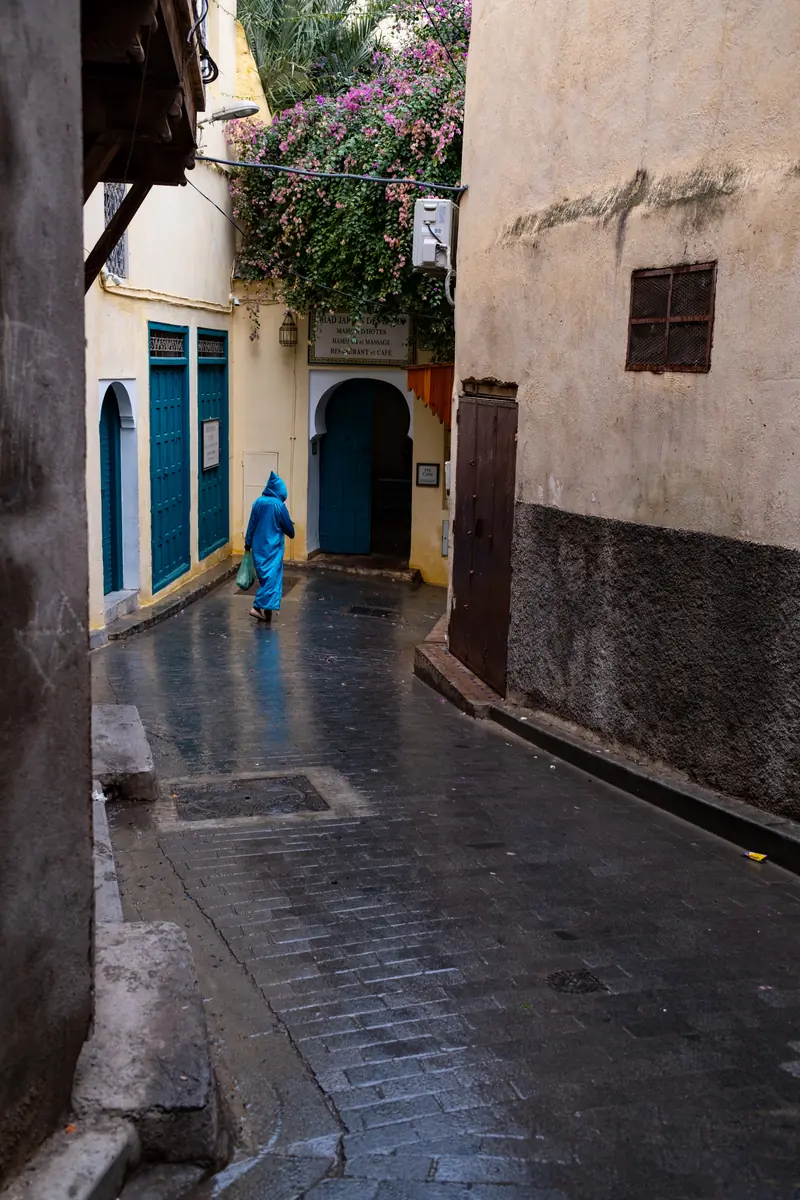 Vicolo lastricato e bagnato con una figura in blu sullo sfondo